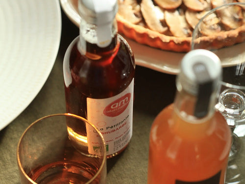 Photo de la tarte aux champignons avec un verre accompagné d'une bouteille de pétillante rhubarbe AM et d'une bouteille de boisson rhubarbe Alain Milliat