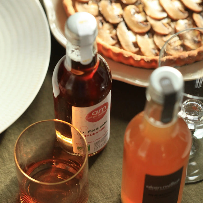 Photo de la tarte aux champignons avec un verre accompagné d'une bouteille de pétillante rhubarbe AM et d'une bouteille de boisson rhubarbe Alain Milliat
