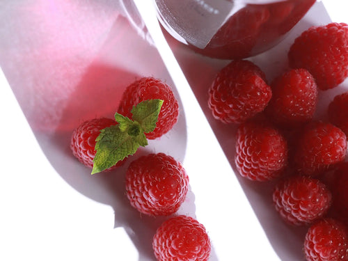 Visuel avec des framboises qui prennent la forme d'une bouteille de pétillante rhubarbe AM et de la boisson rhubarbe Alain Milliat